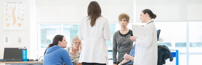 Group of women doctors and nurses having a meeting in a room with bright windows behind them.