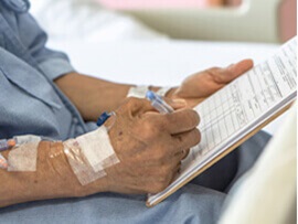 Elderly man's hand with an IV line signing a form.