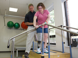 Therapist helping female patient with leg prosthetic use climbing stairs in a therapy session.