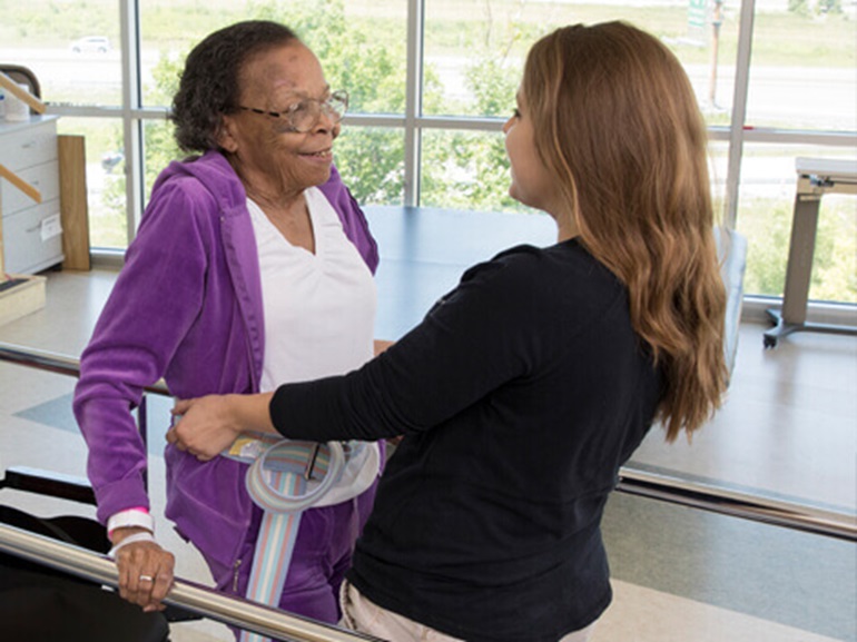 Therapist works with older female patient on balance and walking.