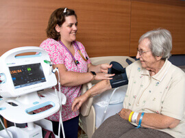 Female nurse in pink scrubs putting a blood pressure cuff on a patient.