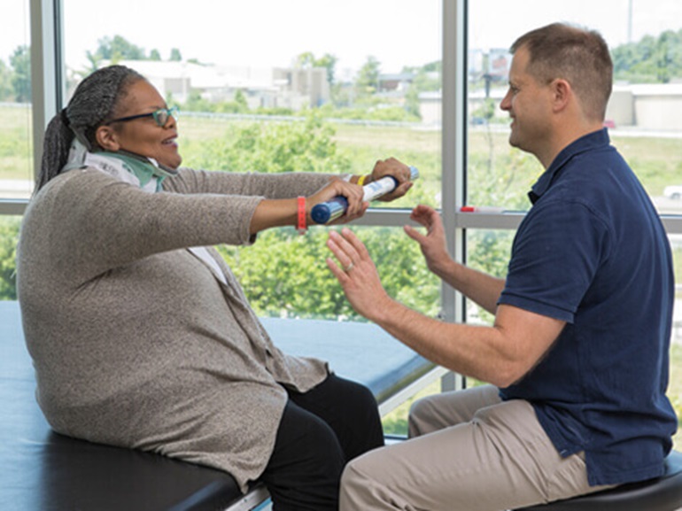 Female patient works on grip strength with a therapist.