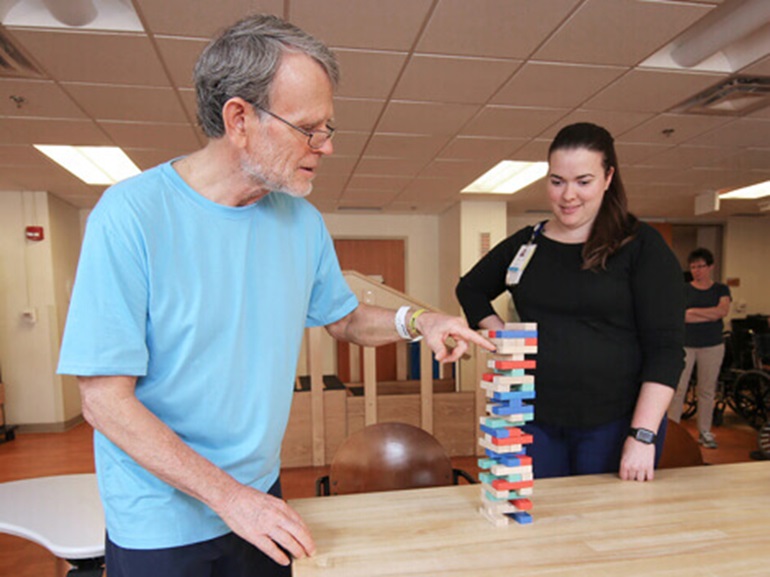 Male patient works on building fine motor skills using small stacking blocks as part of stroke rehabilitation.
