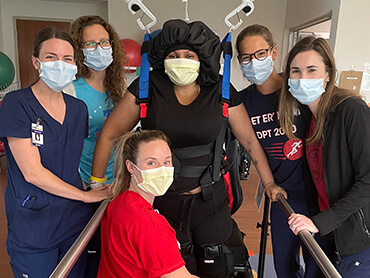 Female patient in an overhead harness surrounded by a group of female therapists.