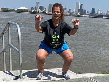 Woman with surgical scars on knees doing a squat in front of a lake.