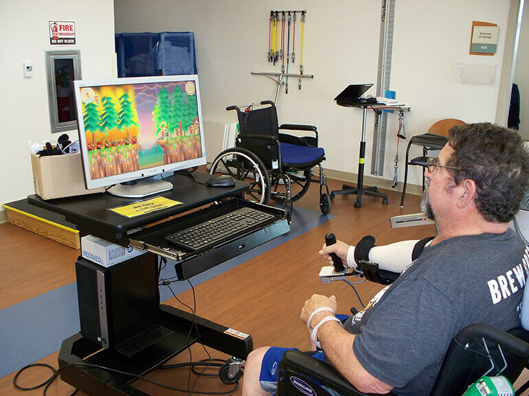 Man sitting in chair and using a gaming joystick to control movements on a computer monitor.