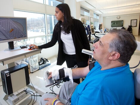 Man with graying hair and using hand-held control to move items on a computer display screen.