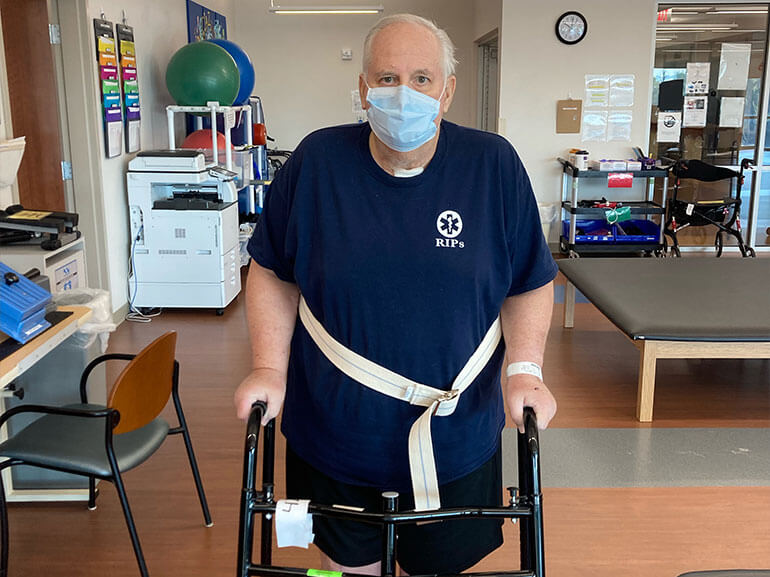 Barry Minnich stands using a walker in therapy.